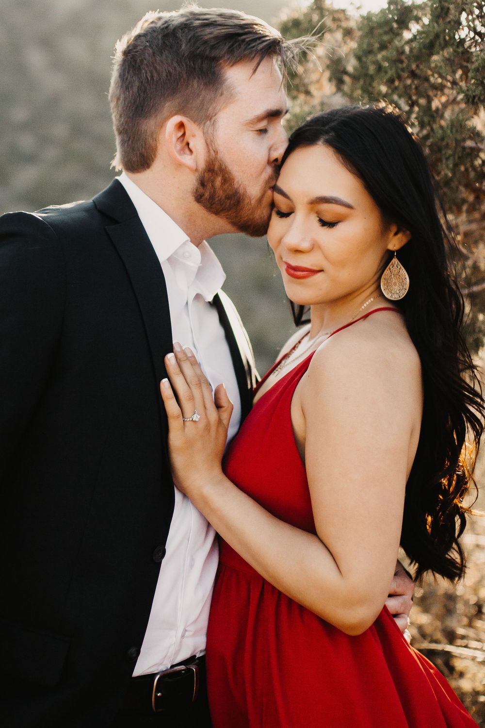 A couple embraces intimately against a natural backdrop in evening light.