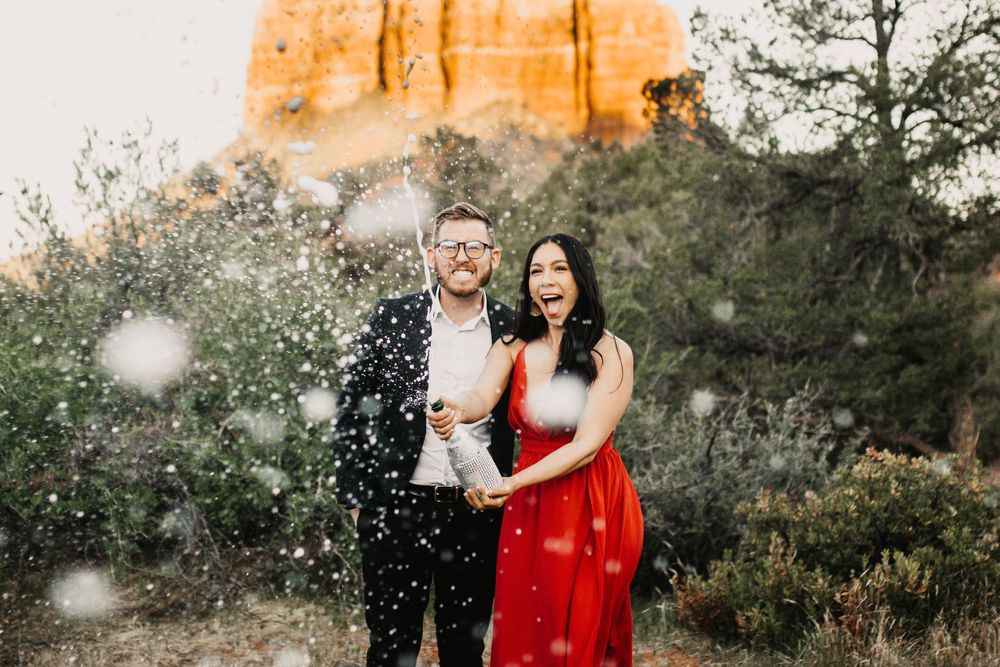 Couple celebrates with confetti during sunset engagement photoshoot in desert landscape.