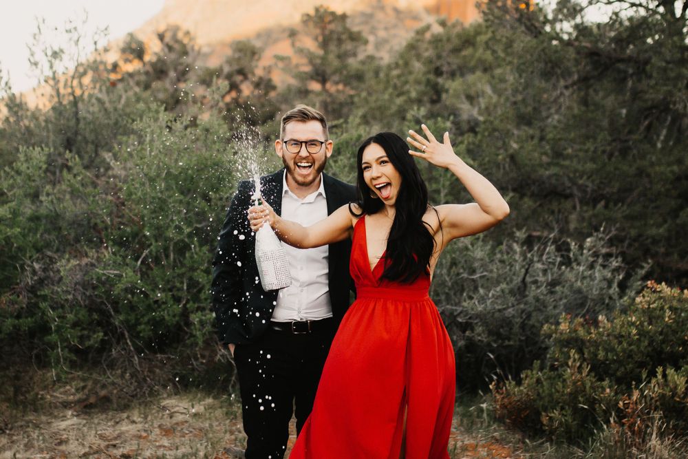Couple poses for engagement photos in desert setting with dramatic mountain backdrop.