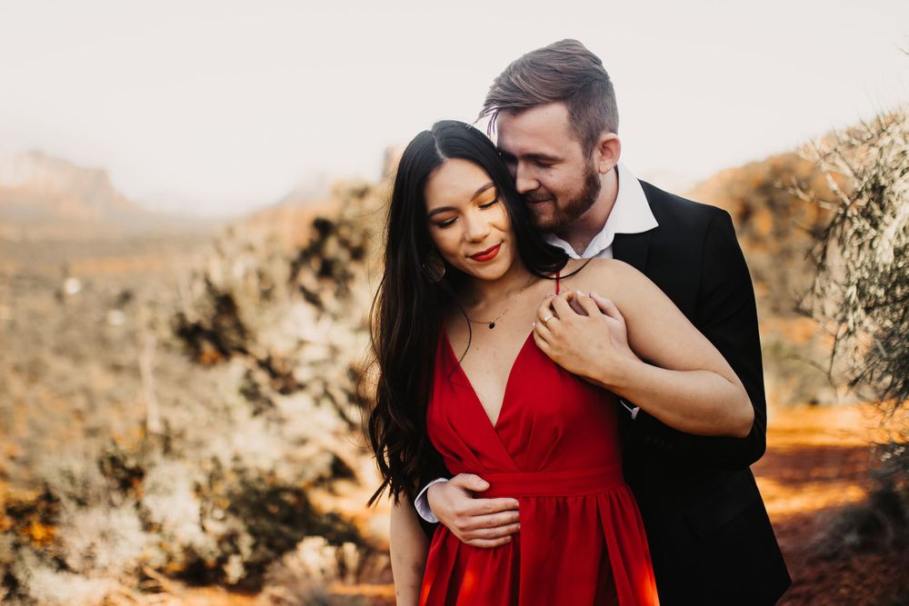 A romantic couple embraces against a desert landscape backdrop during golden hour sunset.