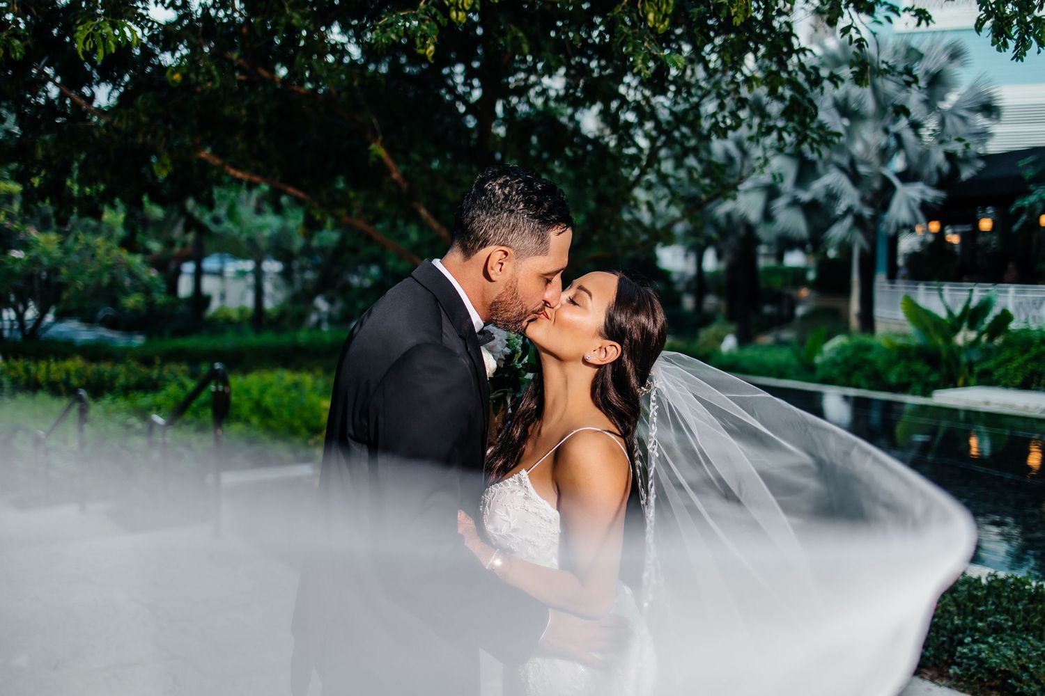 Romantic wedding couple sharing a tender kiss amidst a misty tropical garden setting.