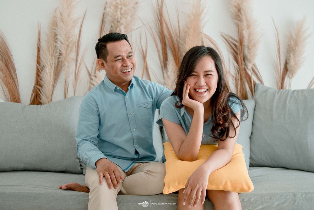 A couple relaxes together on a gray couch with pampas grass decor in the background.