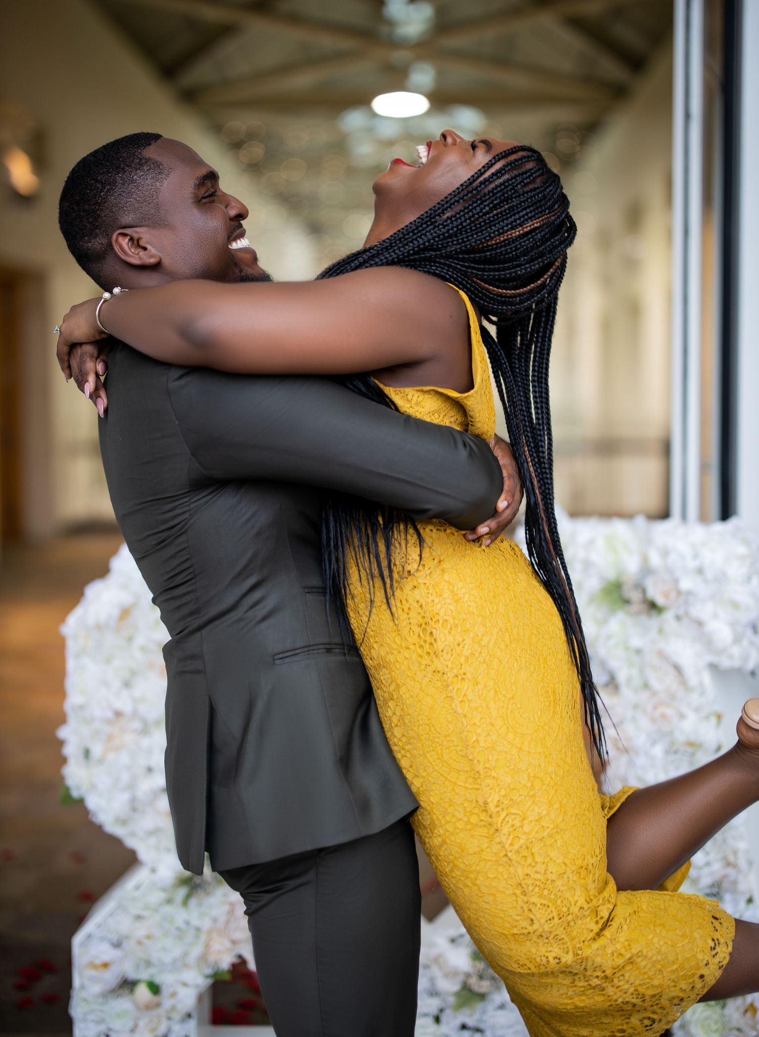 Joyful couple embracing, with person in yellow dress being lifted by partner in grey suit.