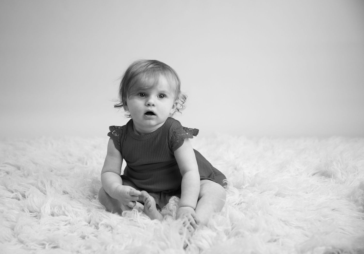 Black & white sitter session. child with curly hair sitting on flokati, playing with her toes
