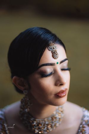Close-up portrait showcasing delicate maang tikka and bridal jewelry with soft makeup.