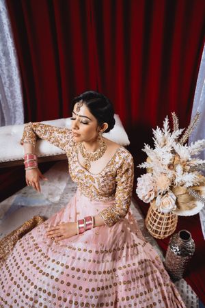 South Asian bride in pink and gold lehenga posed elegantly with dried flower arrangement.