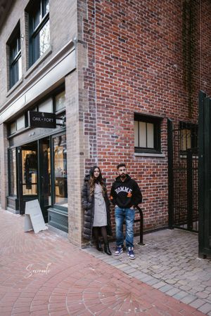 A couple posing against a brick wall outside a storefront in an urban setting.