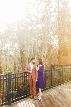A stylish couple poses on a deck with sun-lit trees creating a dreamy background.