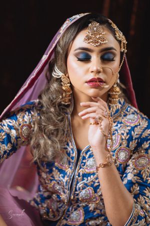 Traditional bridal portrait featuring pink veil, blue embroidered dress and elaborate gold jewelry.