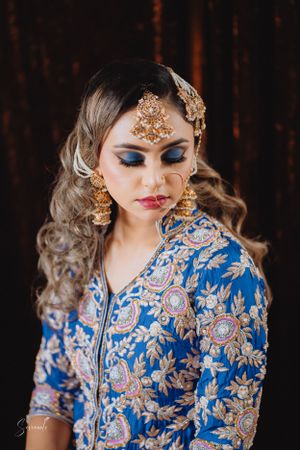 Traditional South Asian bridal makeup and jewelry with intricate gold headpiece and blue embroidered outfit.