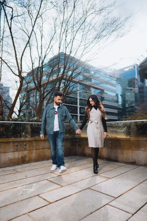 A stylish couple walking together on an urban terrace with modern buildings in the background.