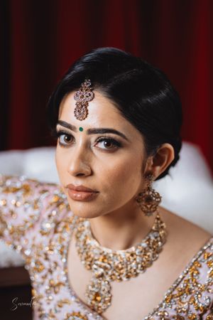 Elegant South Asian bridal fashion with ornate gold jewelry and traditional makeup against red backdrop.