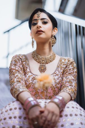 Close-up of traditional bridal jewelry and embellished dress in pink and gold tones.