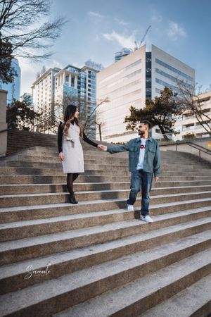 A couple posing on concrete steps with modern office buildings in the background.