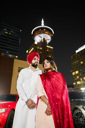 Couple in traditional attire posing at night with Vancouver Lookout tower illuminated behind them.