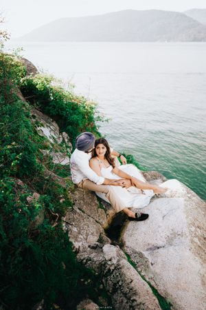 A couple relaxes on rocky coastal cliffs overlooking a serene ocean view.