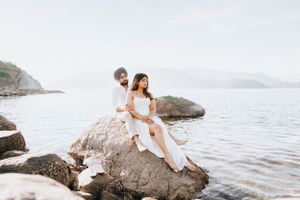 A couple sits together on a large rock formation overlooking a tranquil ocean view.