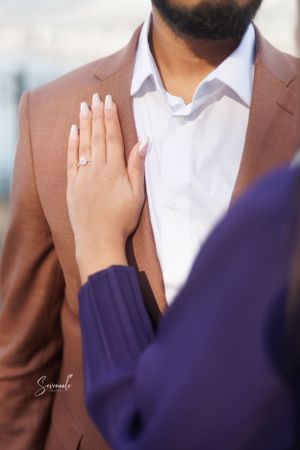 Close-up of hands showing engagement ring against brown suit jacket and purple sleeve.
