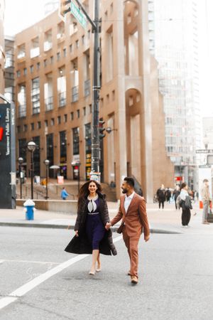 A couple strolls together down an urban street wearing coordinated formal attire.