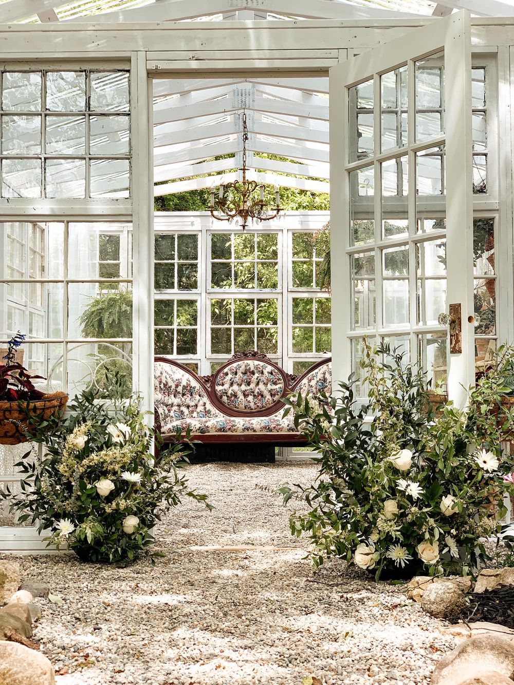 Sunlit greenhouse interior with ornate sofa and white floral arrangements creating an elegant atmosphere.