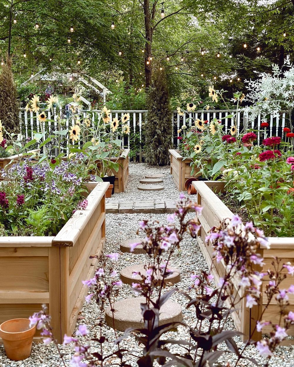 Enchanting garden path lined with raised flower beds and white picket fencing under string lights.