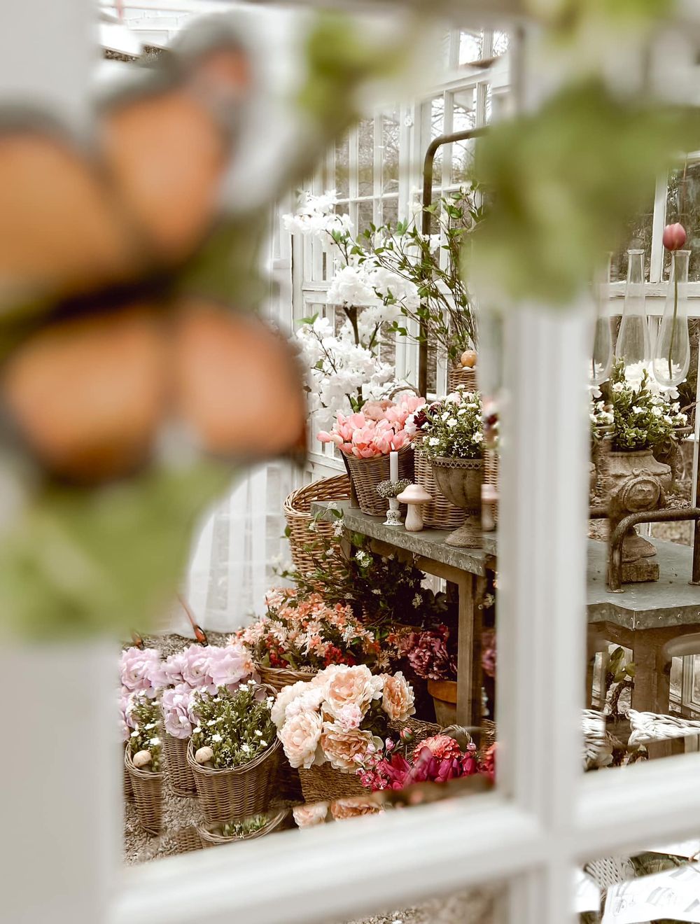 Through a window view of delicate floral arrangements and vintage decor in soft pink hues.