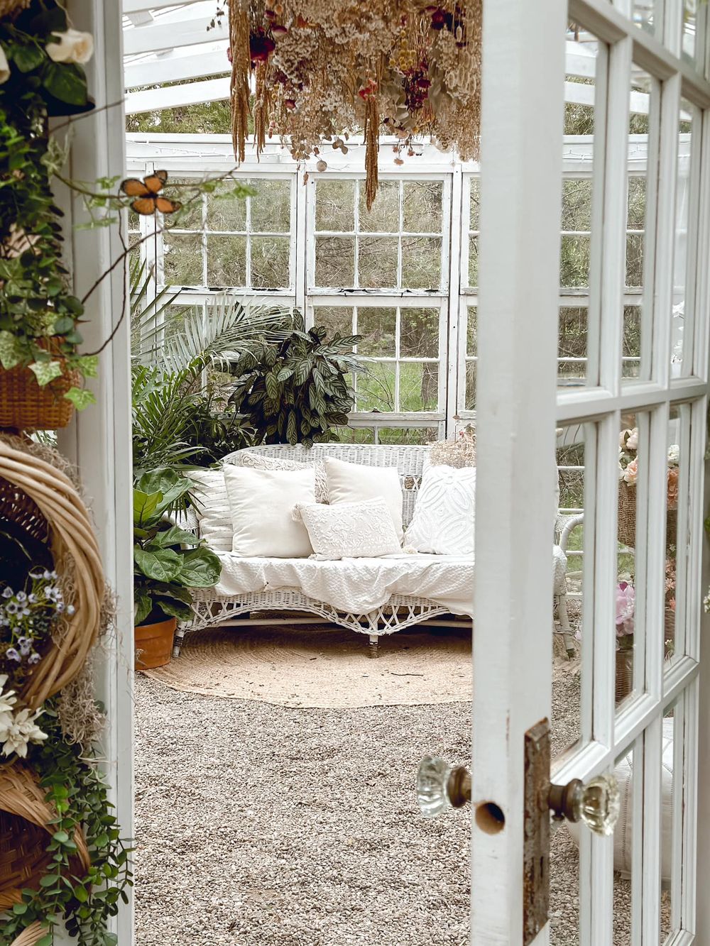 Sunlit greenhouse interior with white wicker furniture and hanging dried flowers creating a peaceful retreat.