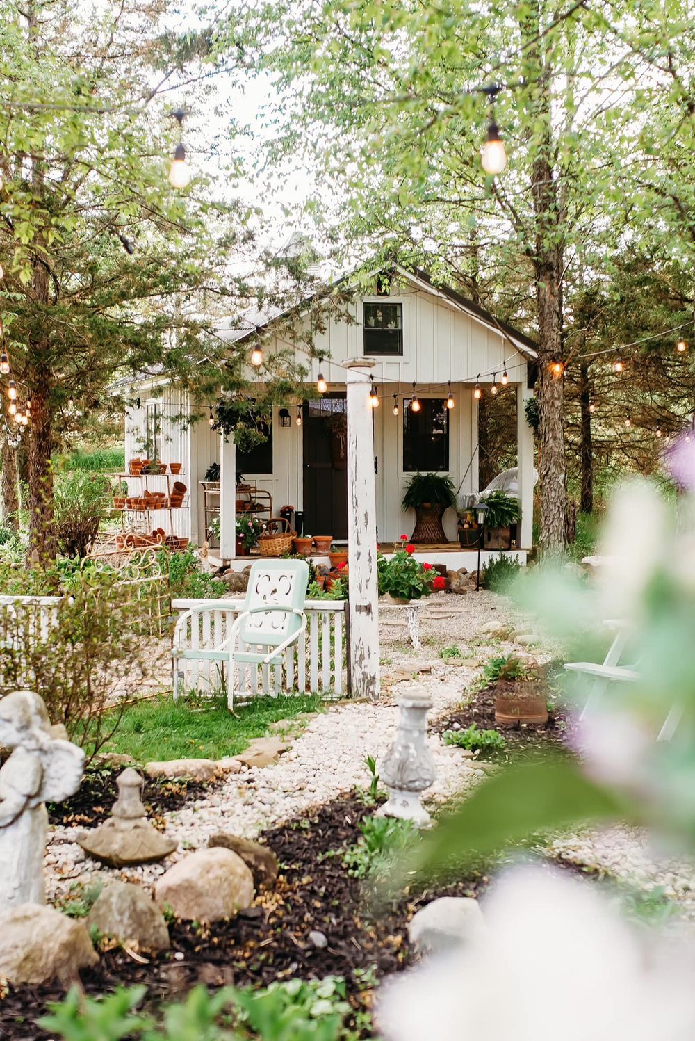 Quaint white garden cottage with picket fence surrounded by lush landscaping and gravel path.