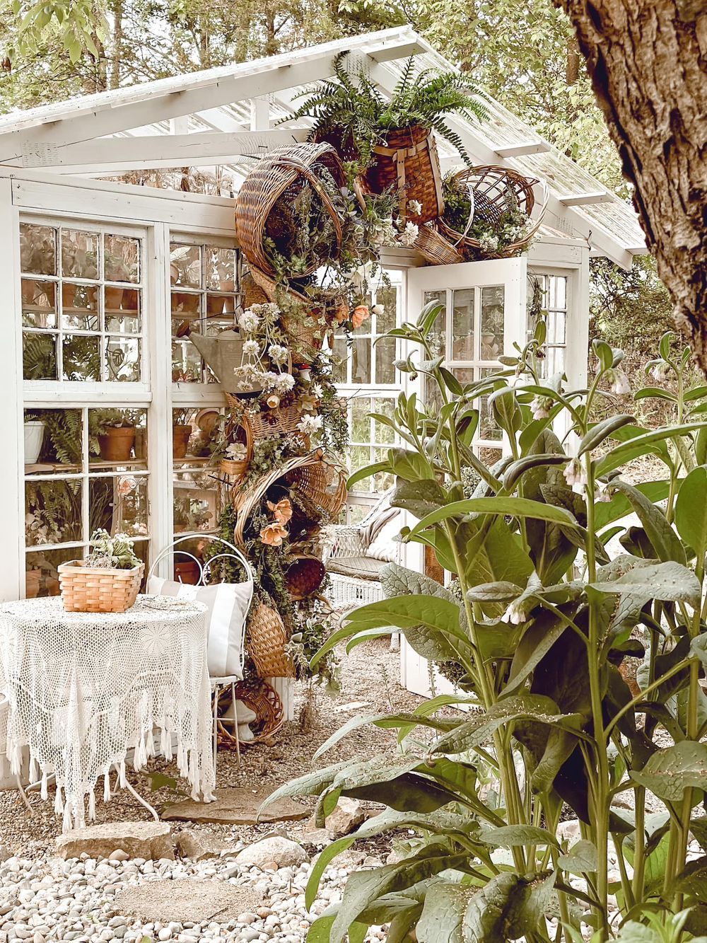 White greenhouse exterior with hanging plants and vintage decor creating a dreamy garden atmosphere.