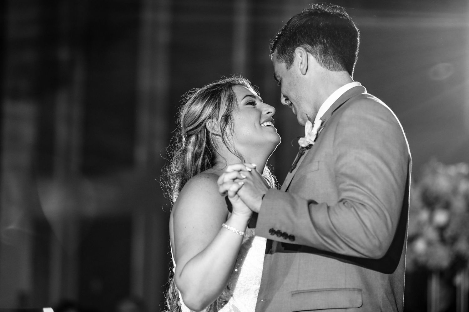 Black and white photo of bride and groom sharing a joyful first dance at their wedding reception.
