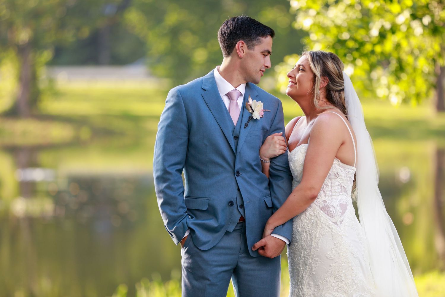 Bride and groom gazing at each other near a serene pond in golden hour wedding portraits.