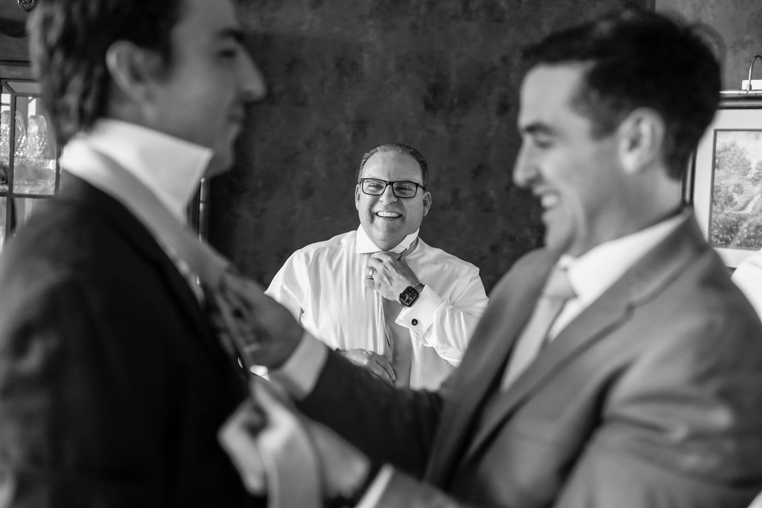Black and white photo of groomsmen laughing and helping each other get ready before the wedding.
