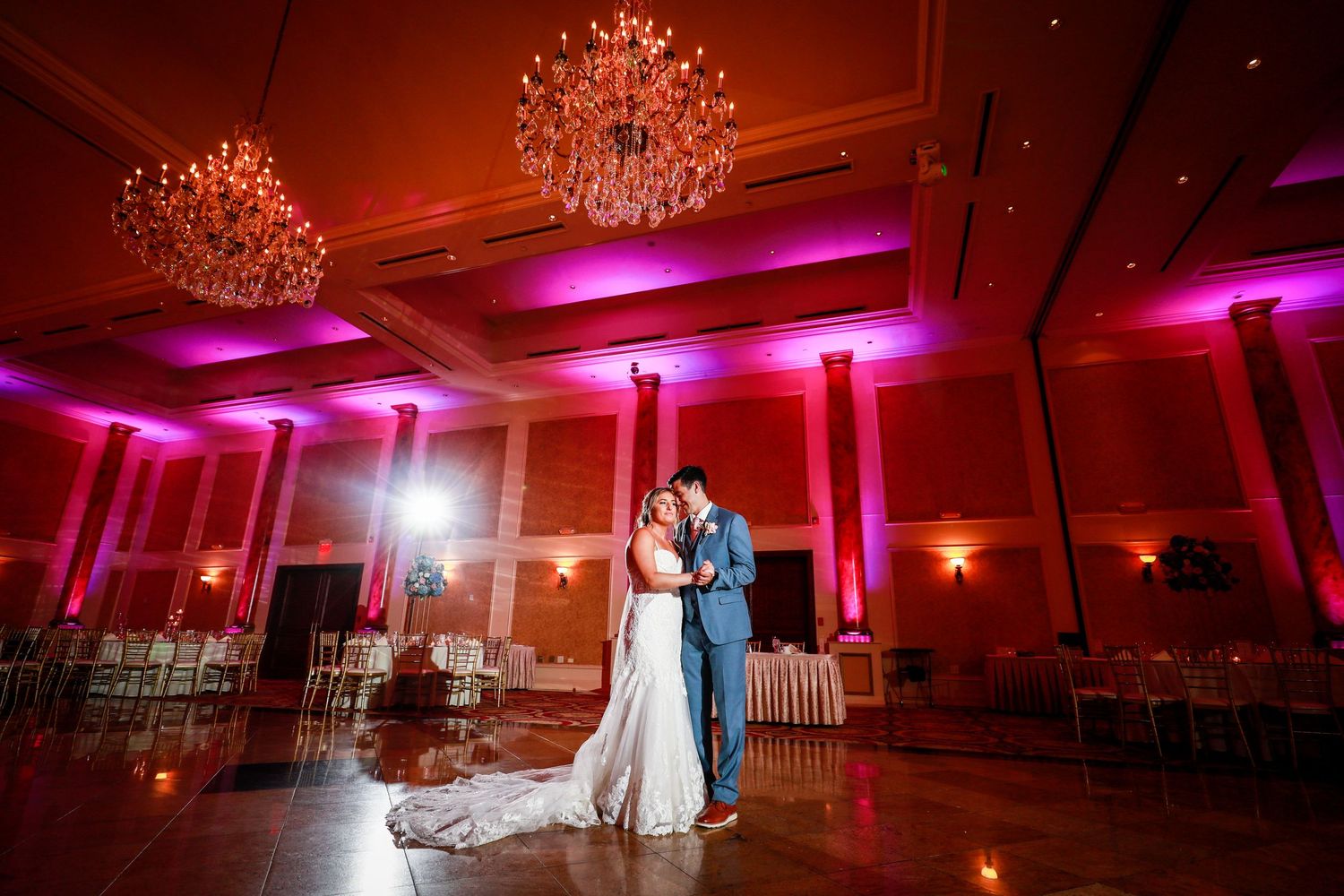 Bride and groom sharing a romantic first dance in an elegant ballroom with pink uplighting.