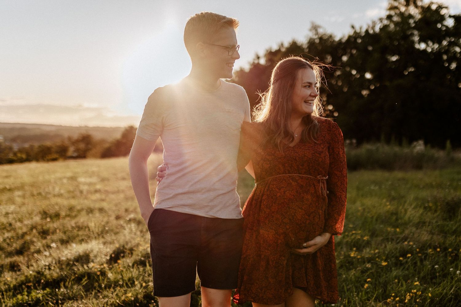 Backlit sunset photo of a couple standing together in a golden field.