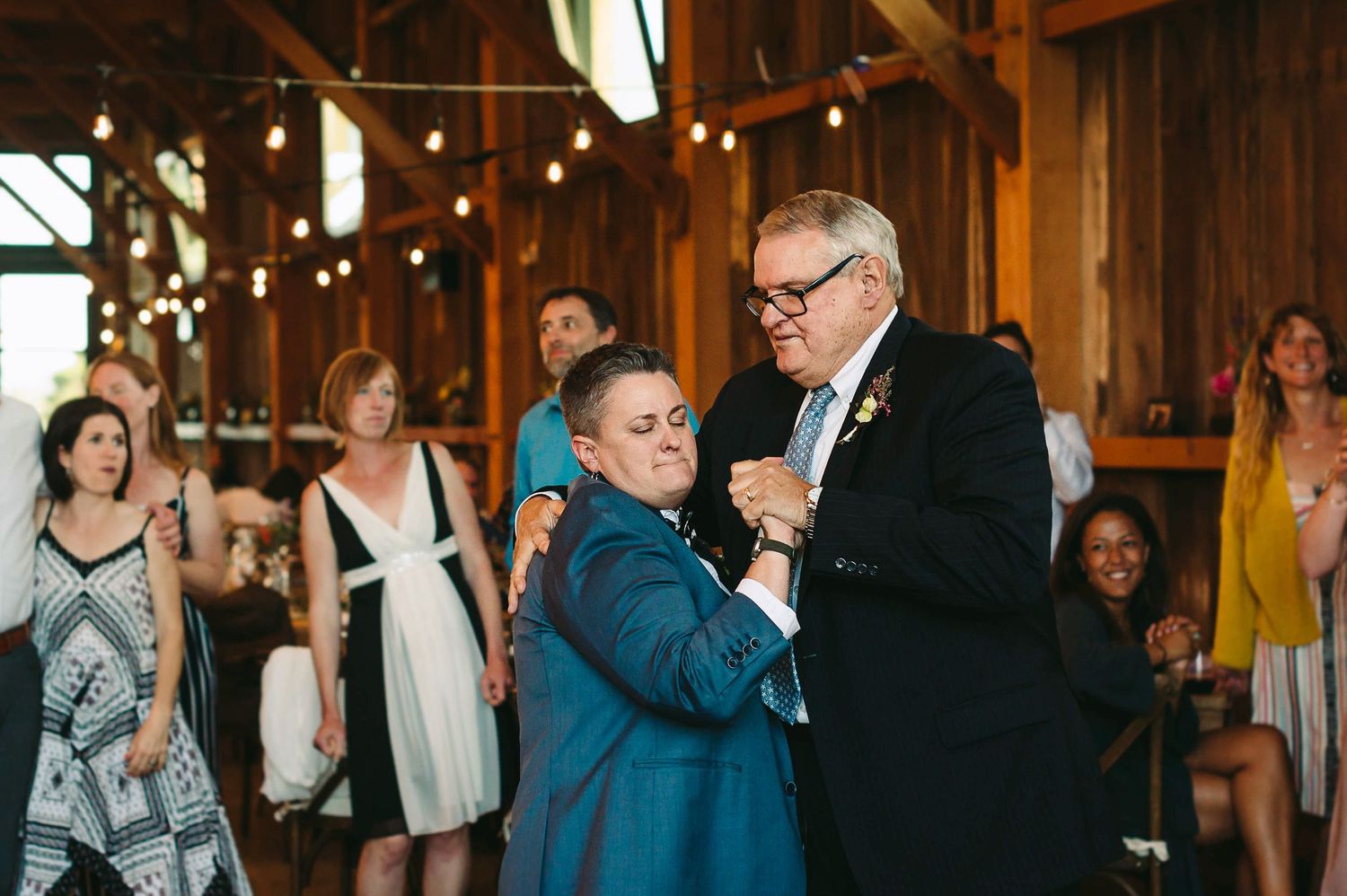 Lesbian bride in a suit dancing with her dad at her wedding reception.
