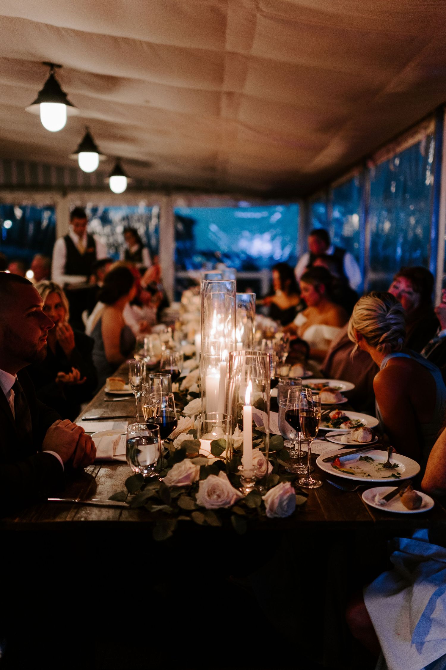 Candlelit wedding reception tables set with elegant place settings in a dimly lit venue.