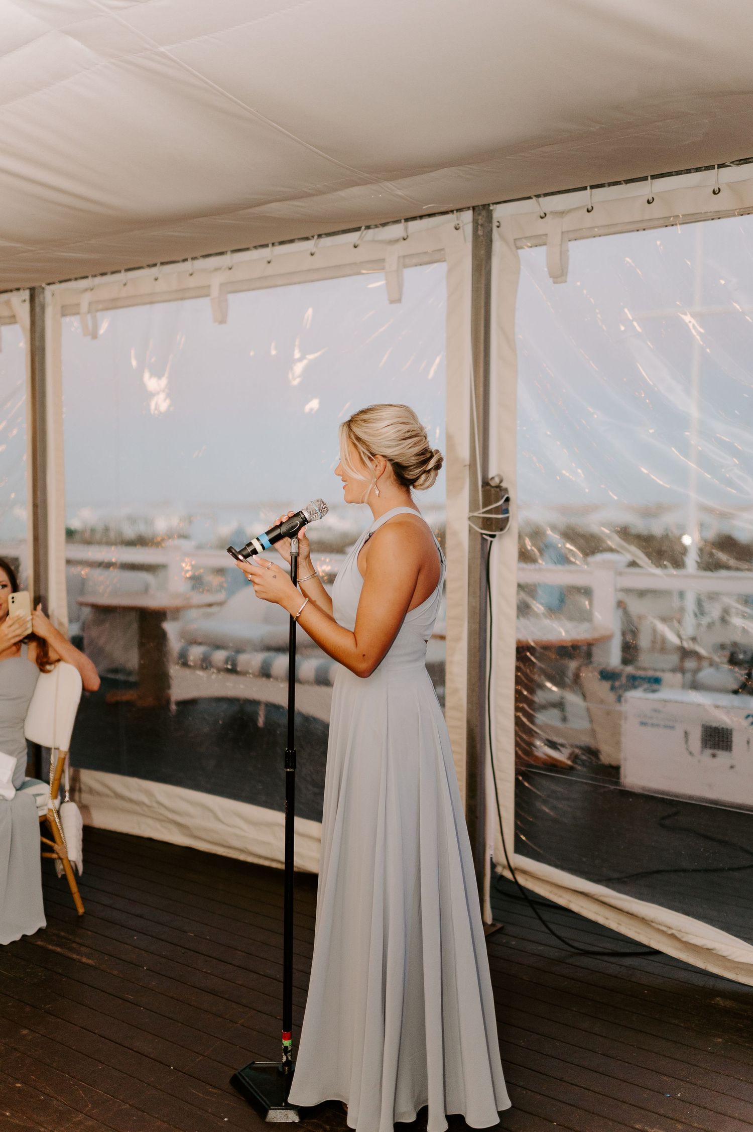 Bridesmaids in light colored dresses pose with champagne bottles against a waterfront backdrop.