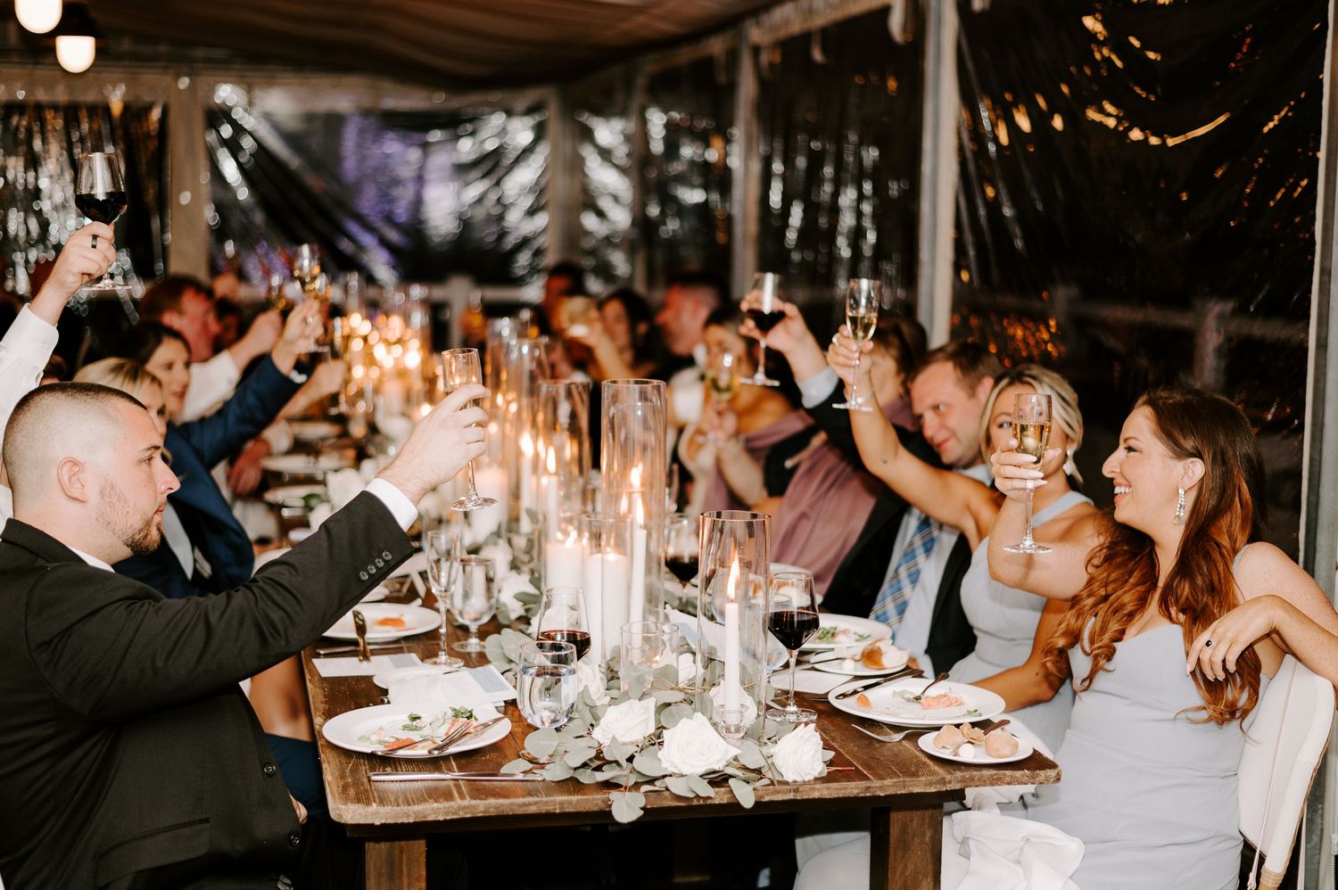 Wedding reception guests celebrate with raised glasses during evening toasts.