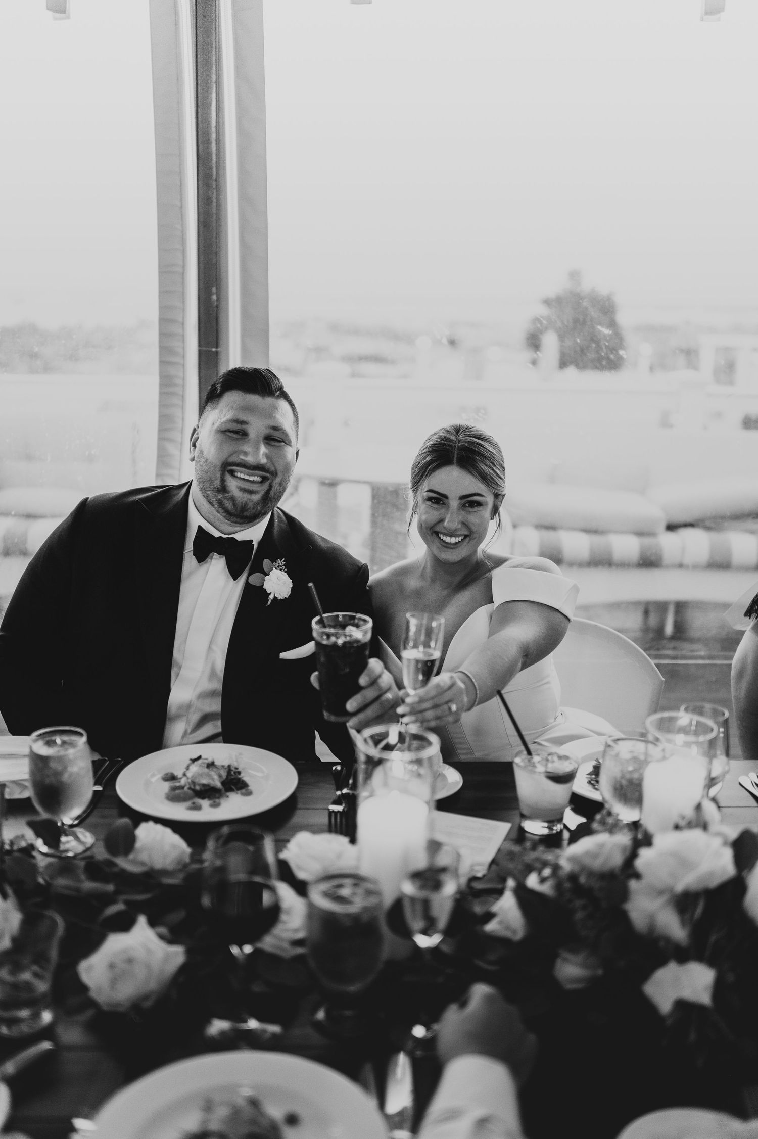 Wedding party members share laughter during dinner at an elegantly set reception table.