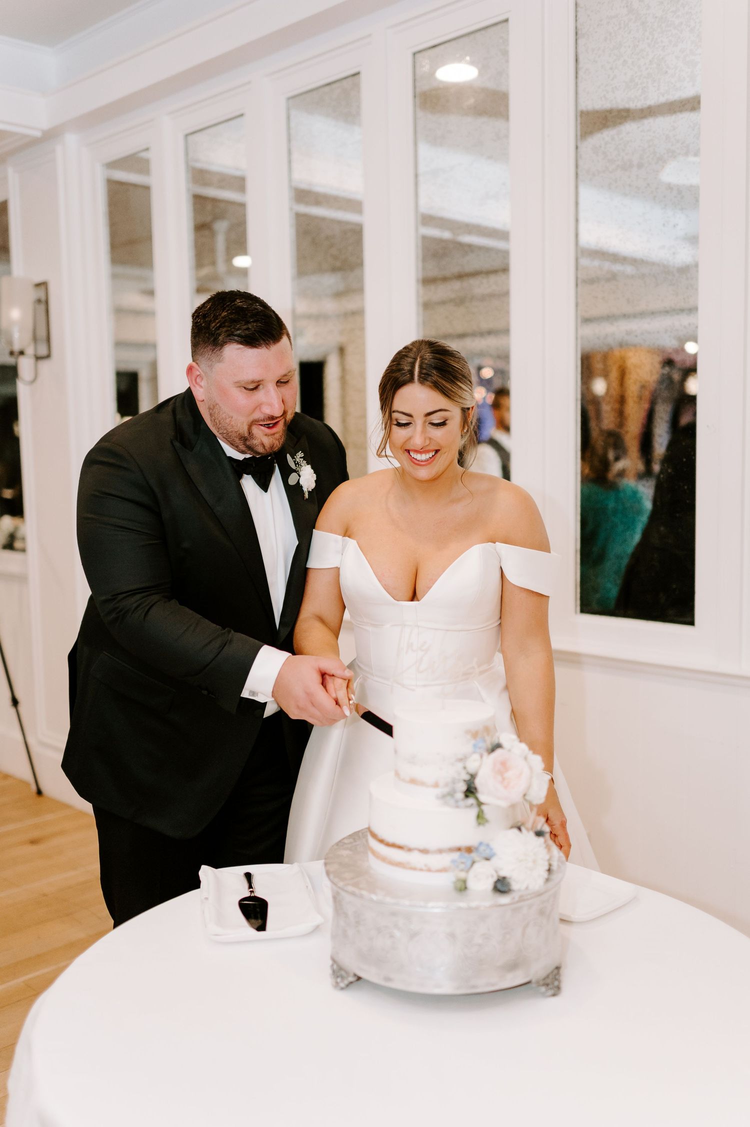Newlyweds cut into their elegant white wedding cake together during their reception celebration.