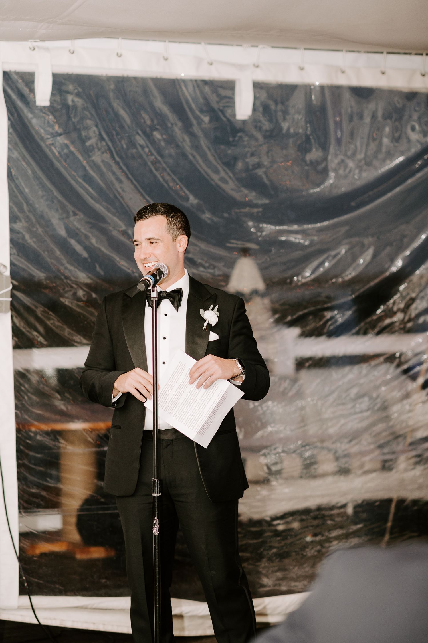 Speaker delivers wedding speech at microphone stand during formal reception.