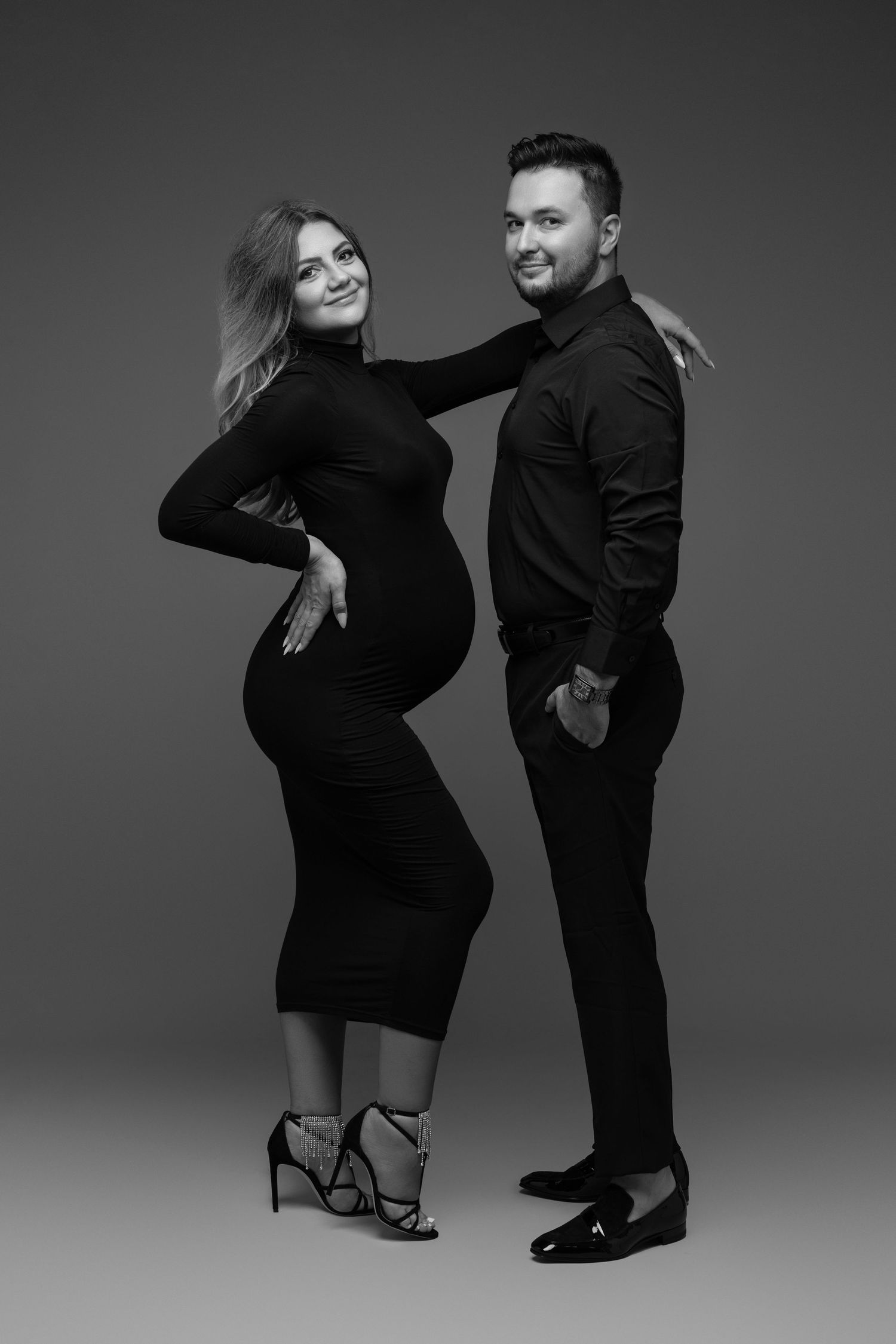 Black and white studio portrait of couple in matching dark outfits.