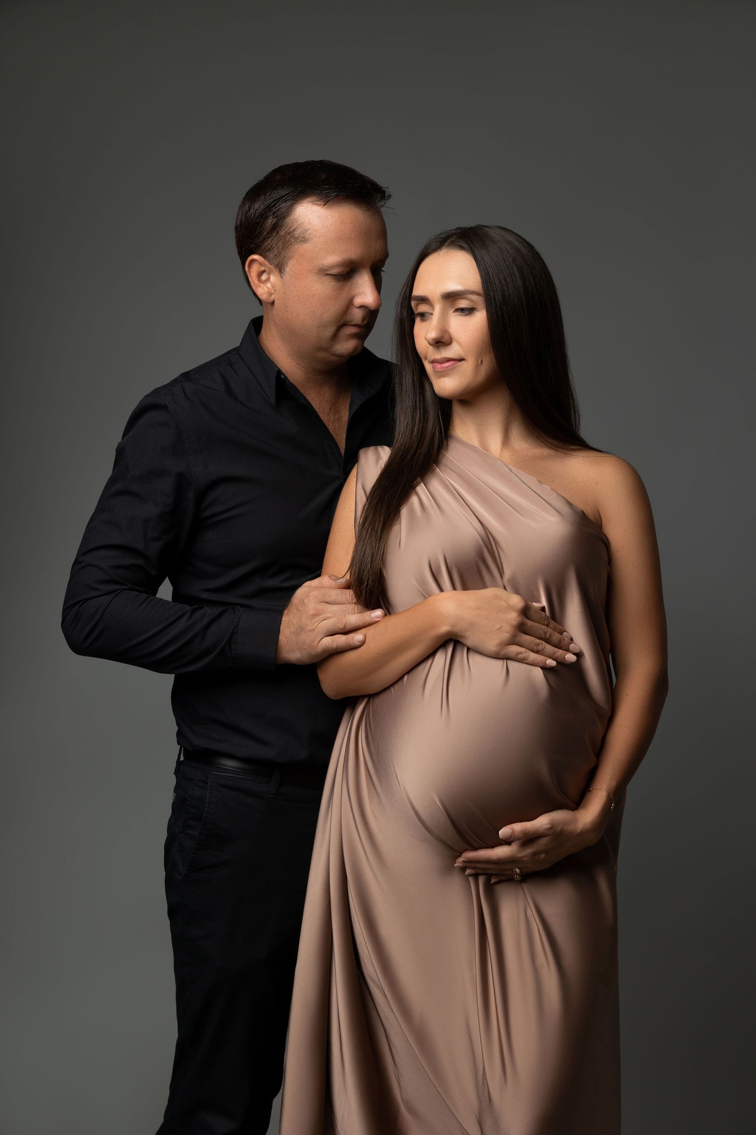 Intimate maternity portrait with couple in coordinated brown and black attire.