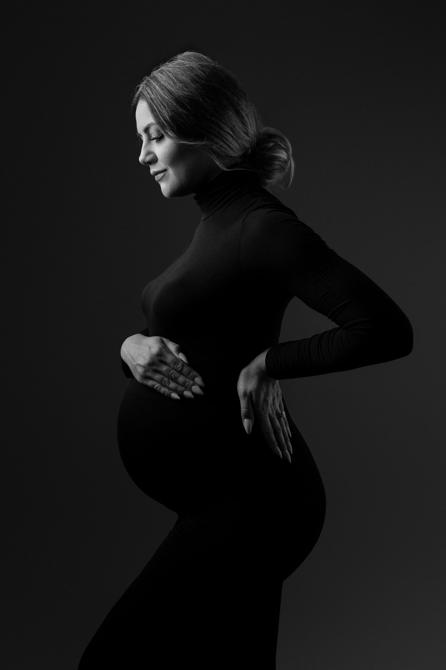Artistic black and white profile of expectant mother in fitted turtleneck dress.
