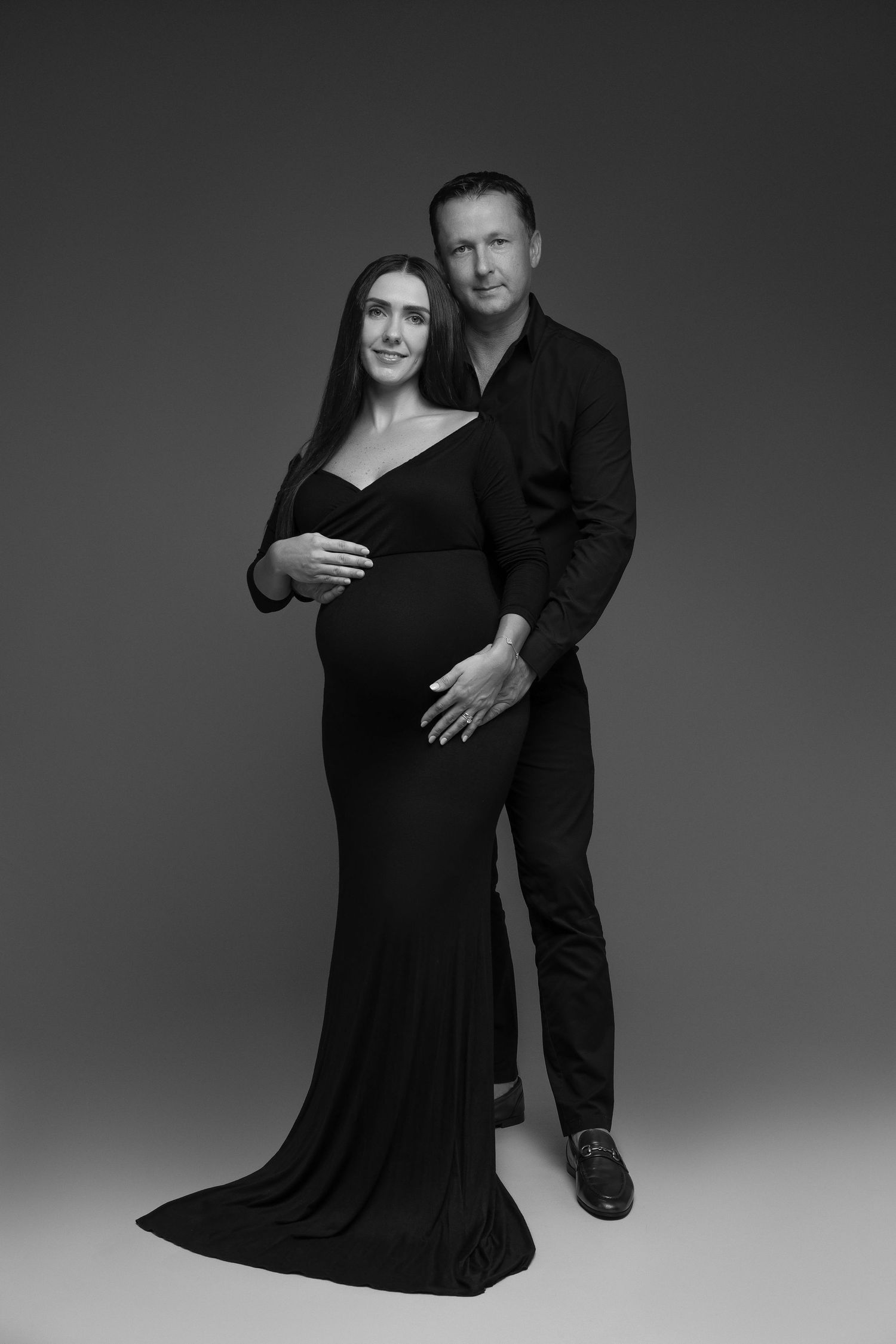 Black and white maternity portrait with couple in formal attire.