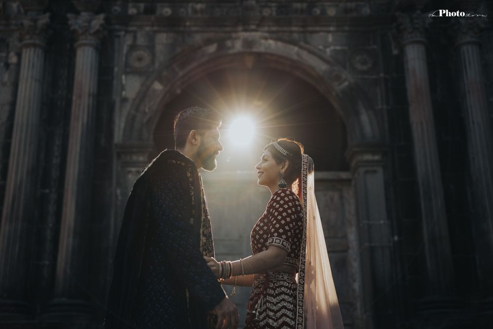 Dramatic backlit wedding portrait with couple standing between pillared architecture.