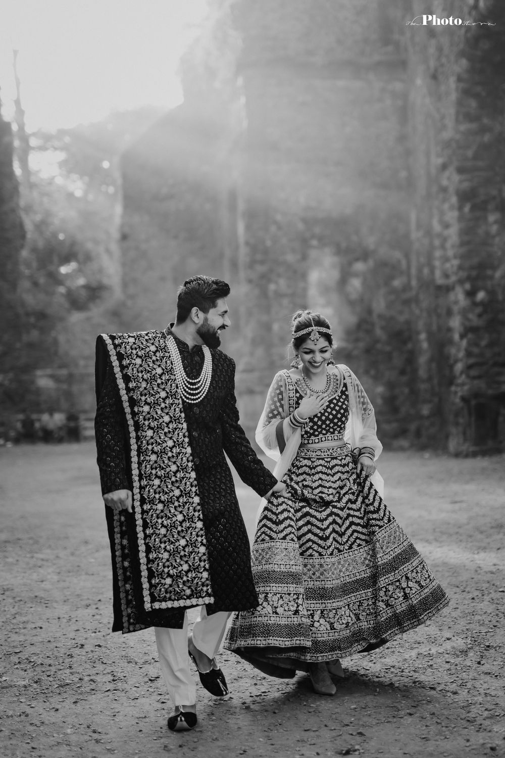Black and white wedding portrait showing couple in traditional Indian attire against stone ruins.