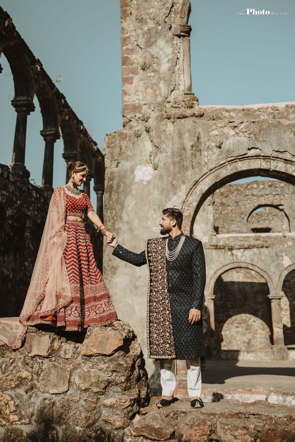 Elegant couple in traditional South Asian wedding clothes pose near stone archways.