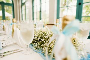 Wedding reception table setting with baby's breath centerpieces and stemware in sunlit venue.