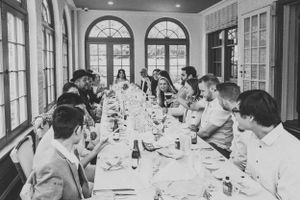 Guests seated at an elegant long dining table in a room with arched windows.